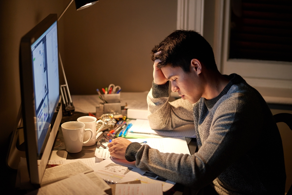 Young man at his computer struggling with college student stress