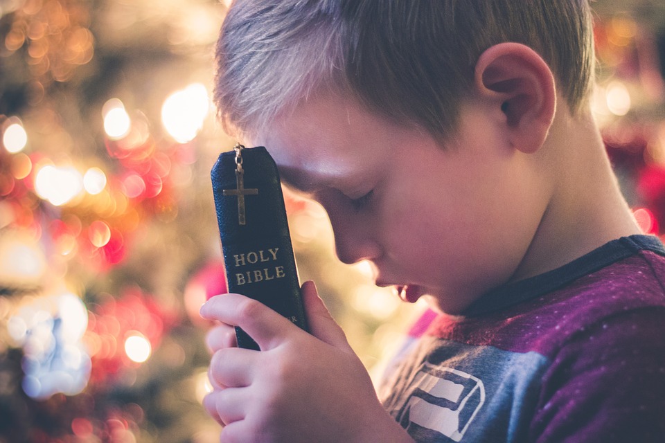 young child holding a Bible and praying